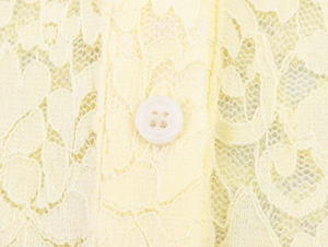 Détail du motif floral en dentelle et du bouton blanc sur un haut à col polo en tricot