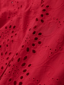 Close-up of red cotton eyelet embroidery fabric with intricate hollowed patterns
