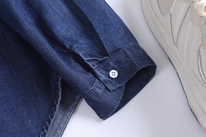Macro shot of dark blue denim shirt cuff with single white button and tidy stitching