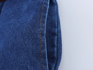 Detailed macro view of deep indigo denim fabric with precise orange contrast stitching