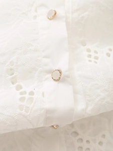 Detail of white cotton eyelet lace embroidery and gold-edged buttons on a long sleeve shirt