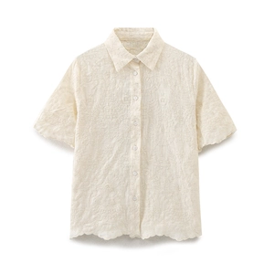 Detail view of the intricate floral openwork embroidery and buttons on the cream shirt