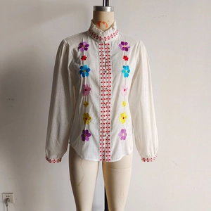 Detail of floral embroidery and ruffle stand collar on a white cotton-linen blouse