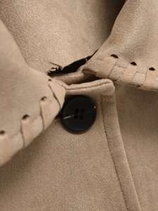 Detail of khaki faux suede jacket featuring black buttons and leather braided seam edges