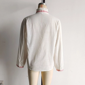 Detail view of the embroidered ruffled collar and back of the white linen shirt