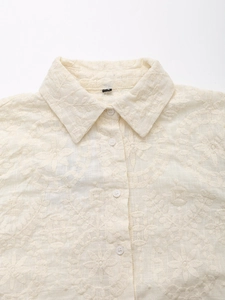 Detailed close-up of ivory embroidered floral pattern and buttons on a summer shirt