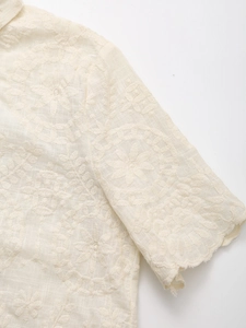 Close-up of summer cream cardigan with floral embroidery and scalloped eyelet sleeve edges