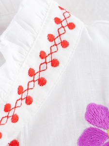 Detailed close-up of delicate floral embroidery and ruffled neckline on a white cotton blouse