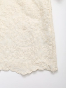 Close-up of floral embroidery detail and scalloped hem on ivory summer shirt fabric