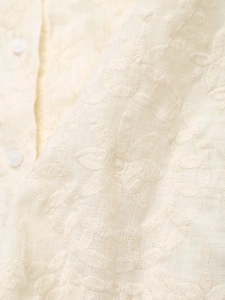 Close-up of ivory summer shirt featuring intricate floral embroidery and small buttons