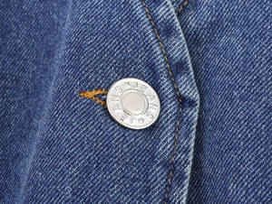 Macro view of a silver metal button with JEANS engraving on blue denim fabric