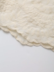 Macro detail of cream embroidered fabric featuring leaf patterns and scalloped edges