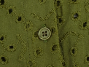 Detailed macro view of olive green eyelet embroidery fabric with a matching button