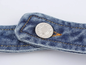 Close-up of a silver metal button with JEANS text and yellow stitching on denim fabric