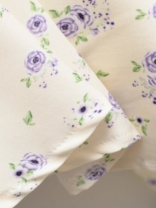 Détail macro du tissu d'une robe avec imprimé floral violet sur fond crème