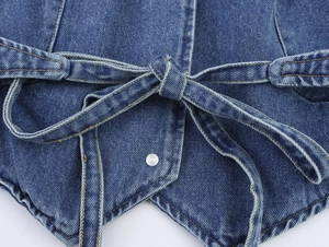 Detail of blue denim vest featuring a waist tie bow and silver metal snap button closure