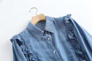 Detail view of denim shirt showing ruffles on shoulders and pearl-like buttons