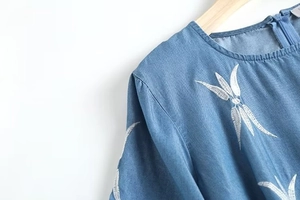 Détail de la broderie florale blanche sur l'épaule de la robe en jean bleu clair