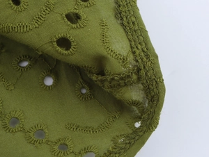 Macro shot of olive green woven cotton fabric with intricate eyelet embroidery details