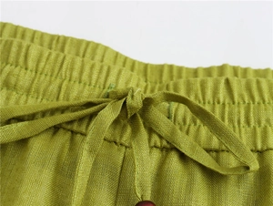 Detailed close-up of green linen trousers' elastic waist with beaded drawstring detail