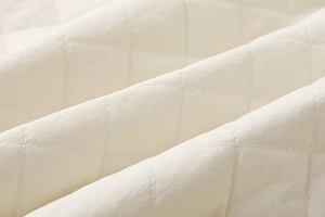 Close-up of cream quilted diamond pattern fabric with detailed stitching and soft texture