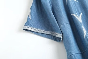Détail d'une robe en jean bleu avec broderies de feuilles blanches et rayures aux manches