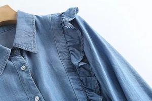 Detail of light blue denim shirt featuring ruffled shoulder trim and pearl buttons