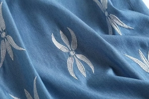 Détail de la broderie de feuilles blanches sur le tissu denim bleu d'une mini robe