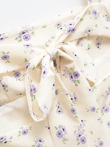 Détail de robe fleurie montrant un grand nœud sur tissu crème aux motifs de roses mauves
