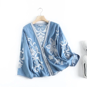 Detailed view of floral embroidery on light blue denim shirt with V-neckline