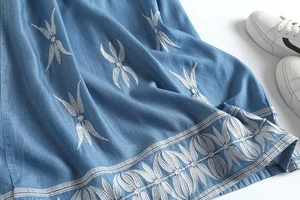 Détail de la broderie de feuilles blanches sur le tissu denim bleu d'une mini robe