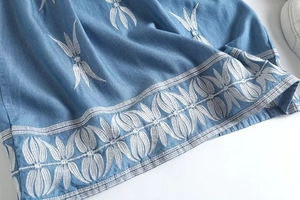 Détail de la broderie florale blanche sur l'ourlet de la mini robe en jean bleu clair