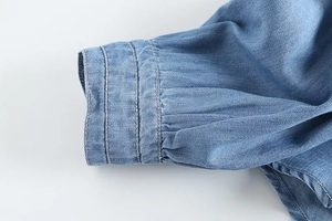 Detail of light blue denim shirt cuff with triple stitching and pleated sleeve design