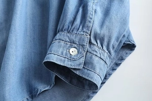 Close-up detail of light blue denim shirt cuff with a white pearl button and stitching