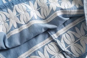 Gros plan sur les broderies florales blanches de la robe courte en denim bleu clair
