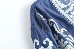 Detail shot of white floral embroidery and delicate lace trim on blue denim shirt