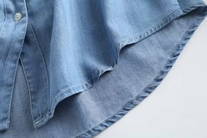 Close-up of light blue denim shirt curved hem showing white stitching and pearl button