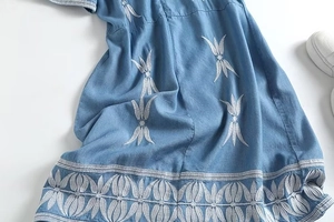 Détail de broderie de feuilles blanches sur robe en jean bleue avec basket élégante