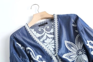 Detailed close-up of vintage floral embroidery and white lace on blue denim shirt