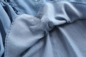 Detail of light blue denim fabric with ruffle trim and button on a casual shirt