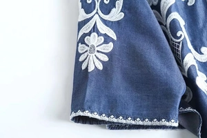Detail of white flower embroidery and wavy lace trim on blue denim fabric sleeve