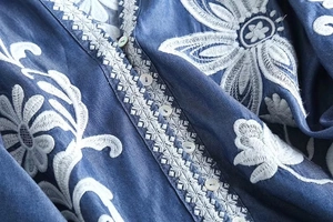 Detail of floral embroidery and white buttons on dark blue denim shirt fabric