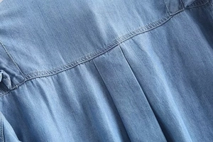 Detailed view of the pleated back yoke and fine double stitching on a blue denim shirt