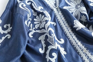 Detailed close-up of intricate white floral embroidery on dark blue denim shirt