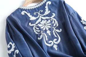 Detailed embroidery on a navy denim blouse with white floral patterns and lace trim