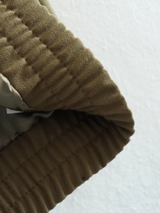 Macro shot of olive green quilted jacket detailing with ribbed cuff and silk lining texture