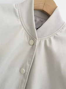 Close-up of ribbed stand collar and matte snap buttons on a beige Y2K bomber jacket
