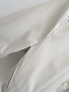 Macro shot of off-white Y2K bomber jacket fabric with smooth finish and matching button detail