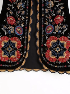 Détails de la broderie florale colorée et bordure dorée sur ce gilet en velours noir