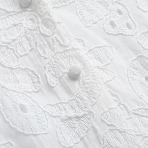 Détails de broderie florale blanche et boutons recouverts de tissu sur une robe en coton